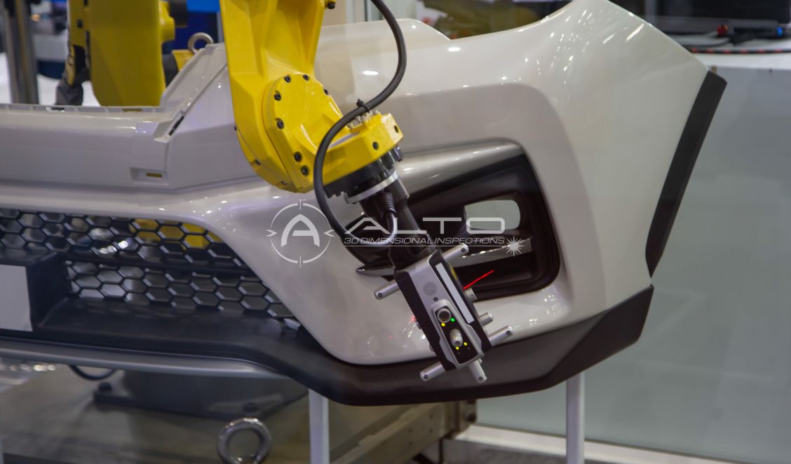 A yellow robotic arm works on a white car bumper, using precise tools such as the Leica AT960 for assembly or inspection in an industrial or automotive manufacturing setting.