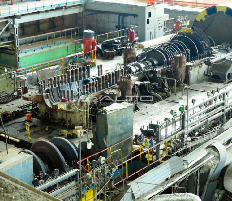 A massive disassembled turbine rotor resting horizontally on supports within a large industrial workshop hall.