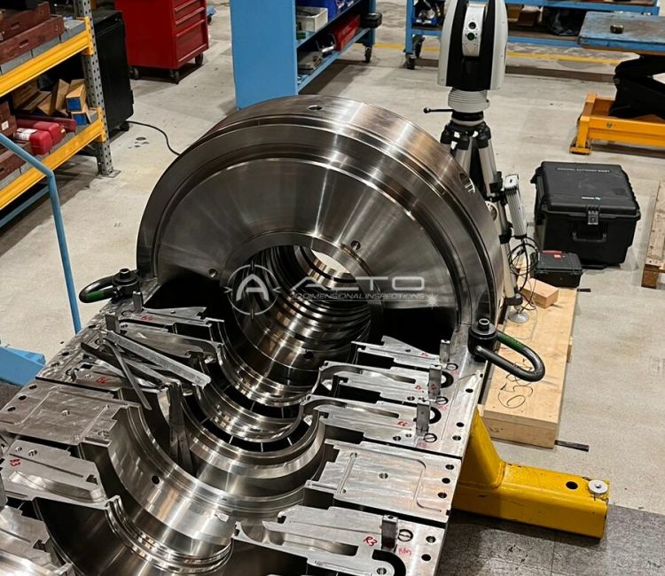 A Leica Absolute Tracker AT960 positioned on a tripod behind a large machined turbine diaphragm for real-time alignment verification.